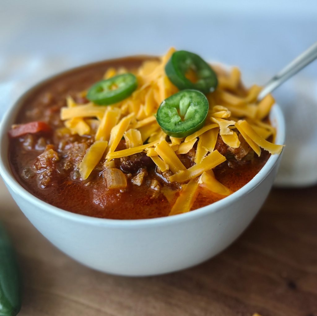 bowl of homemade chili with jalapenos and shredded cheese