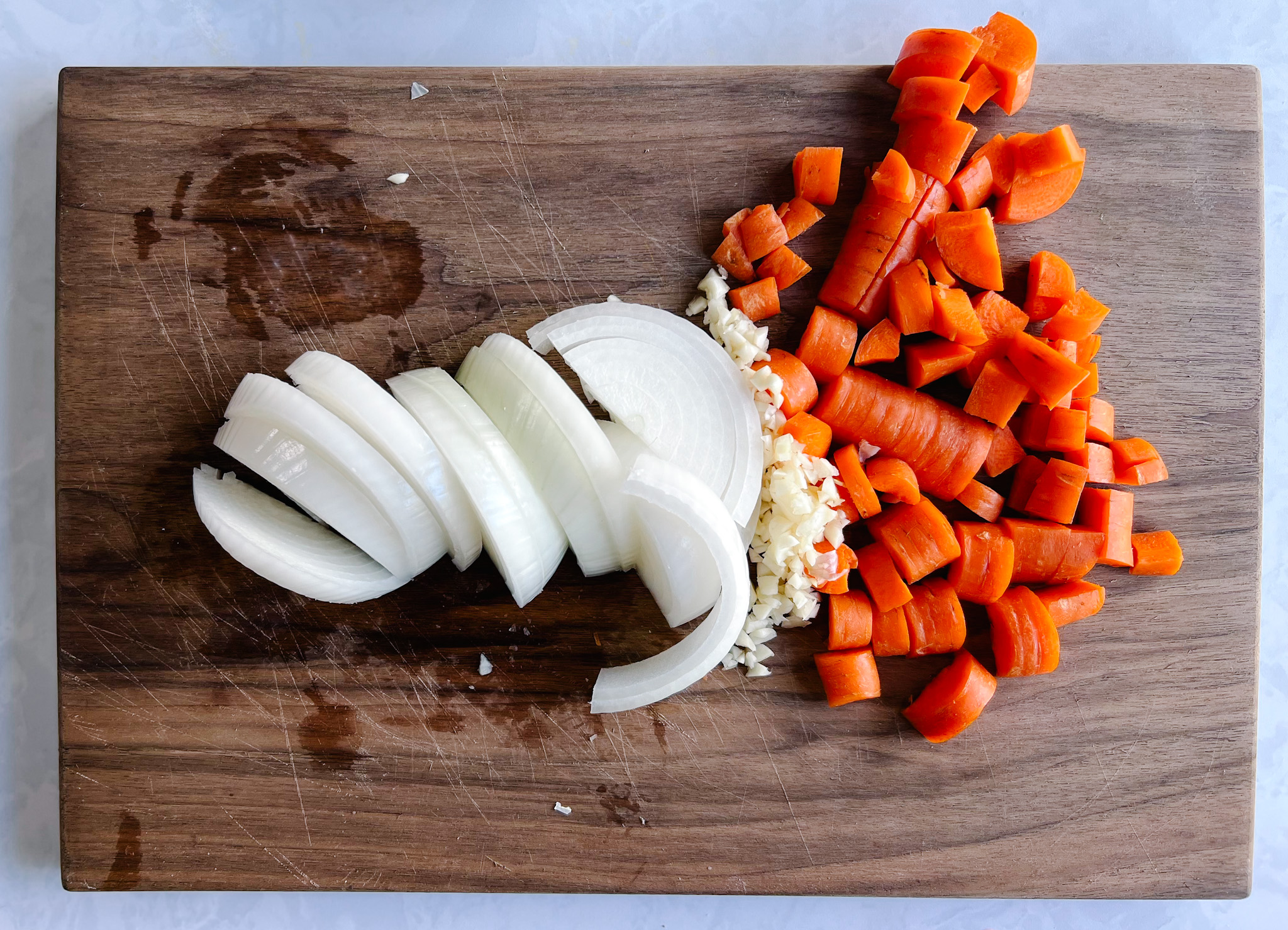 chopped carrots, minced garlic, sliced white onion on cutting board