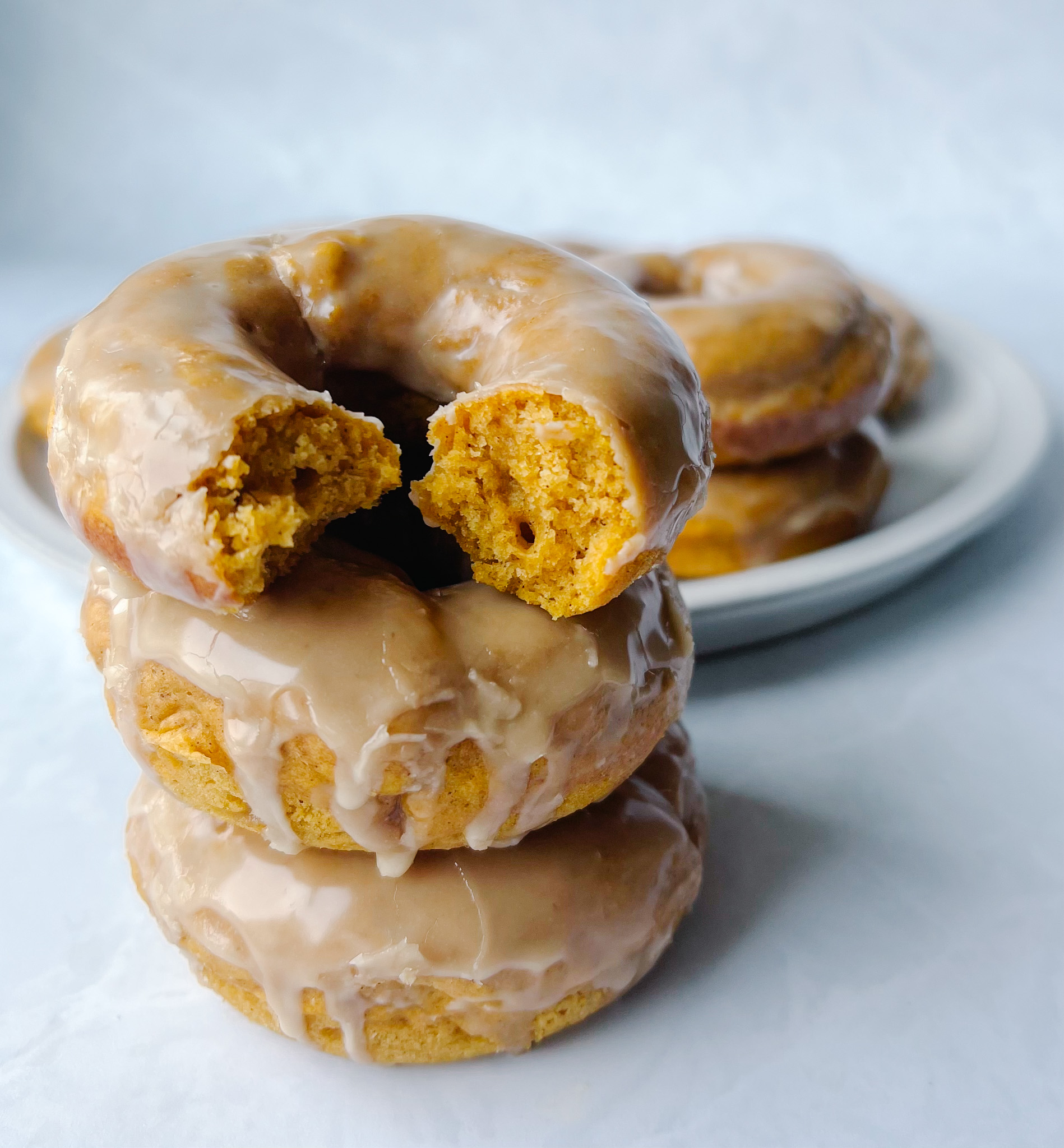 stack of baked pumpkin doughnuts with maple glaze with a bite taken out of the top doughnut