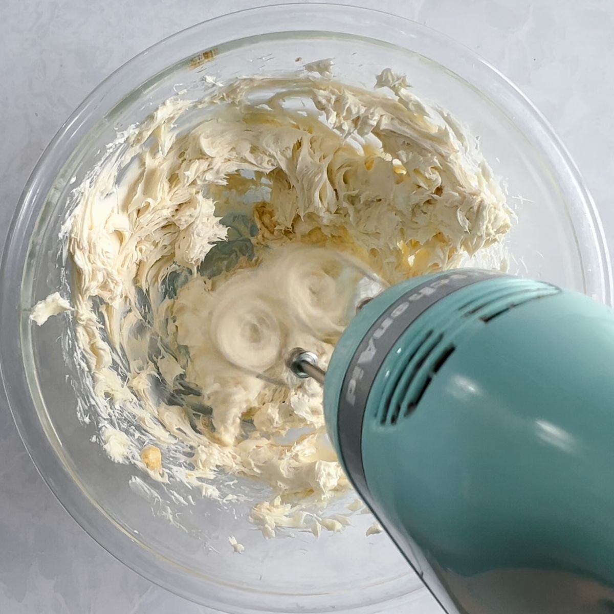 Mixing cream cheese, butter, and vanilla extract with a hand mixer. 