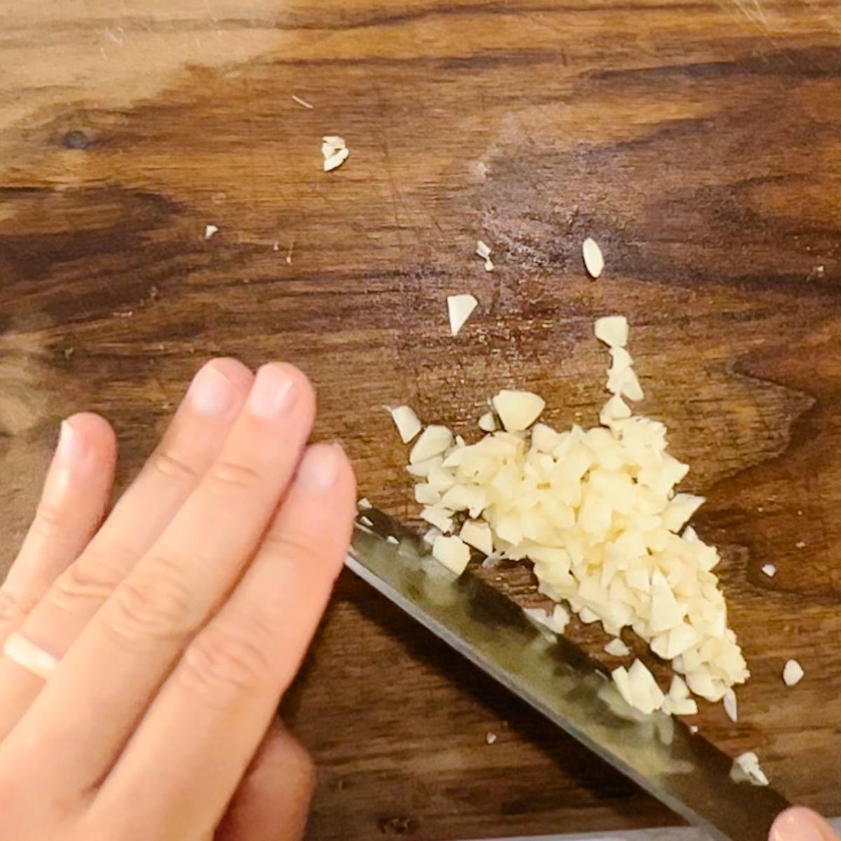 mincing garlic on a wooden cutting board.