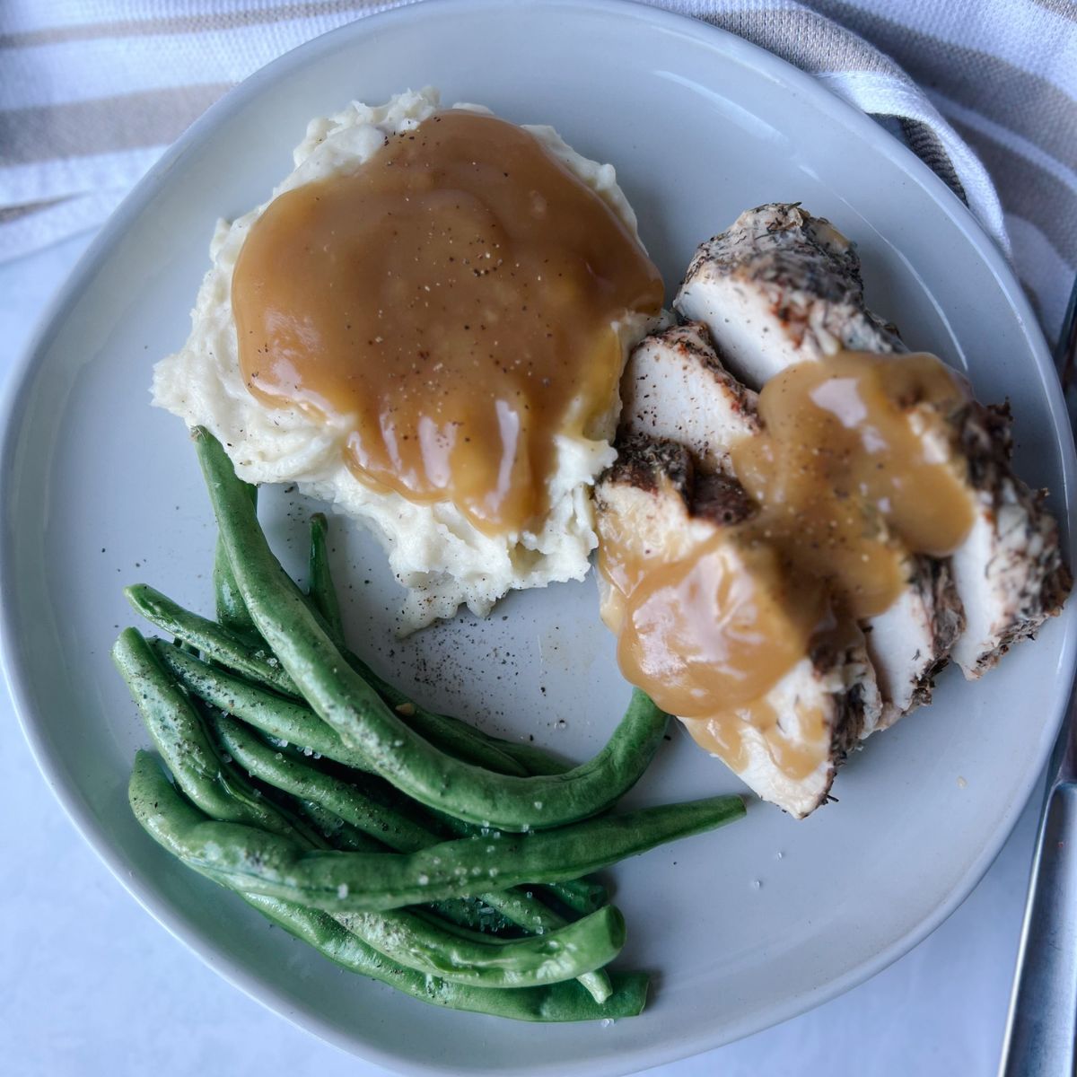 mashed potatoes and gravy, turkey tenderloin with gravy on top, and green beans all on a plate.