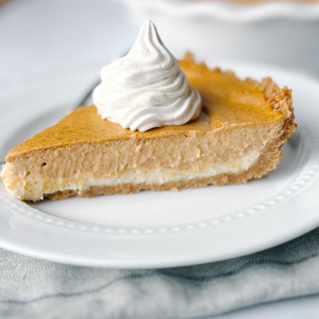 A piece of double-layer pumpkin cheesecake topped with whipped cream.