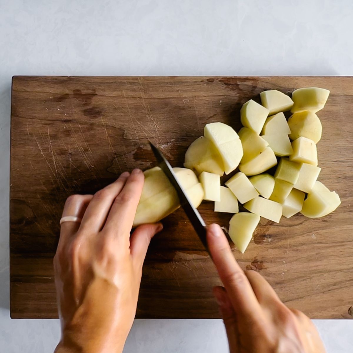 Dicing potatoes into inch long pieces on a cutting board.
