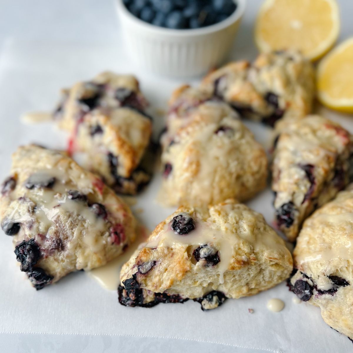 lemon blueberry scones on parchment paper with lemons and blueberries in the background.