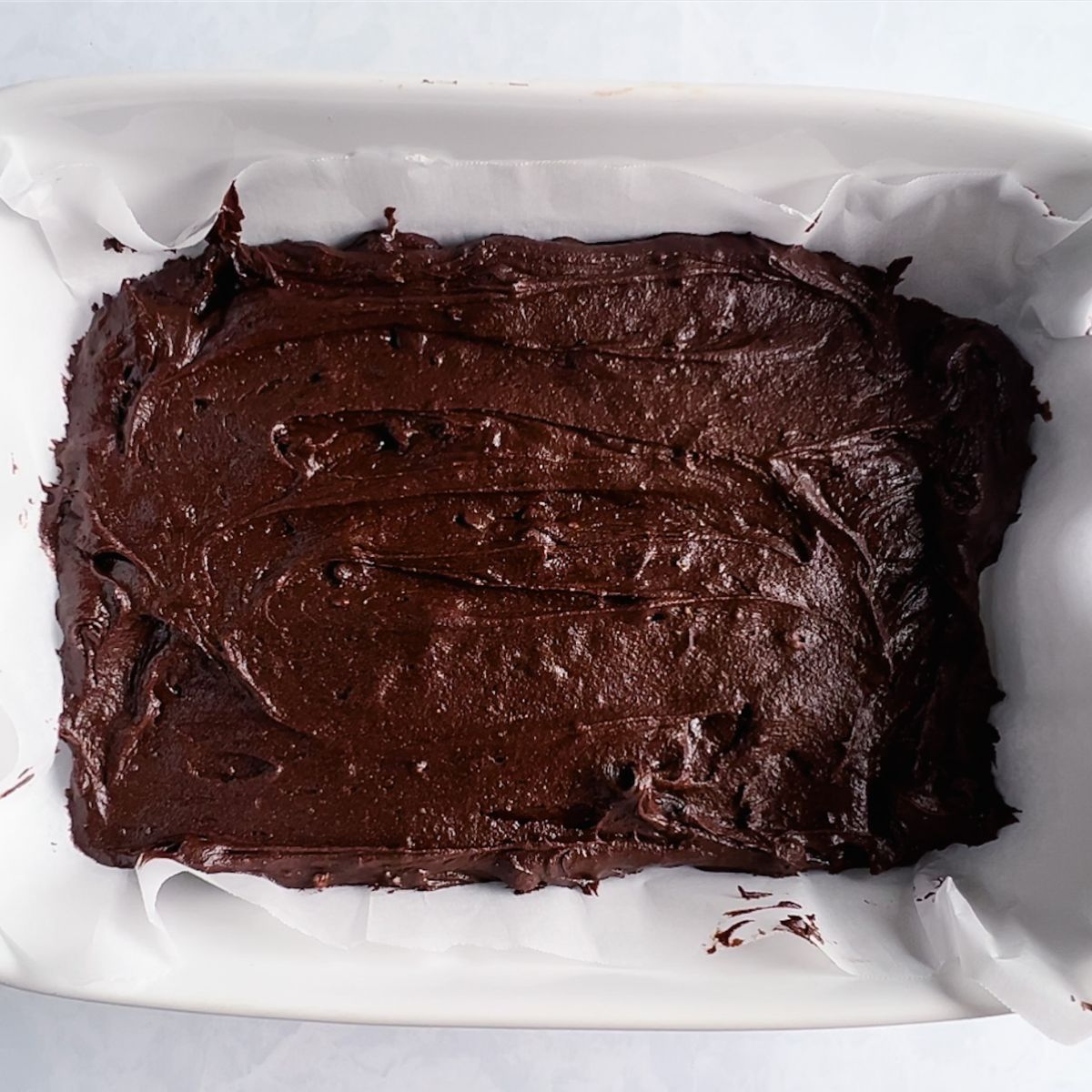 Brownie batter in a 9x13 baking dish on top of parchment paper.