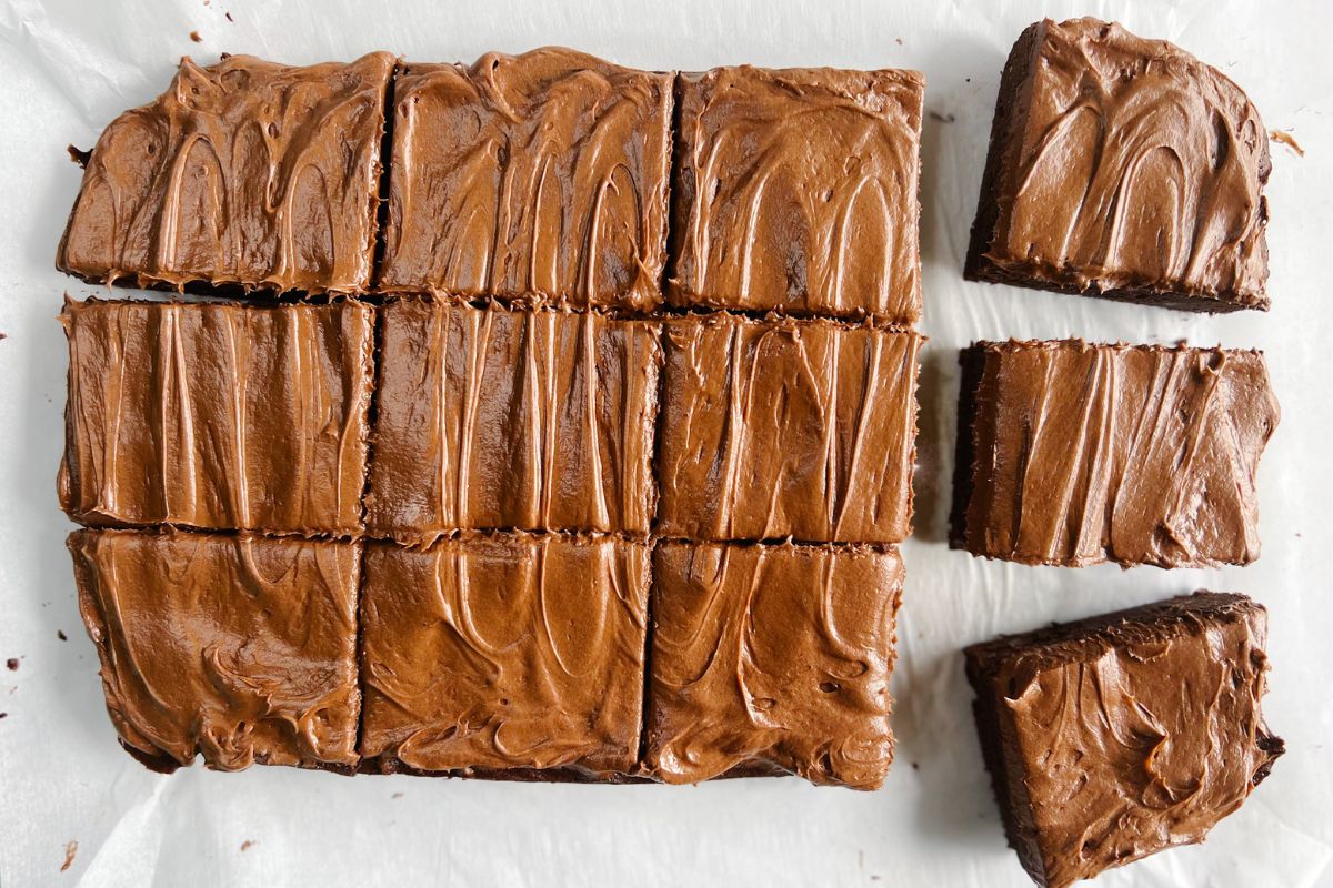 Old-fashioned brownies frosted sitting on parchment paper cut into 12 pieces.