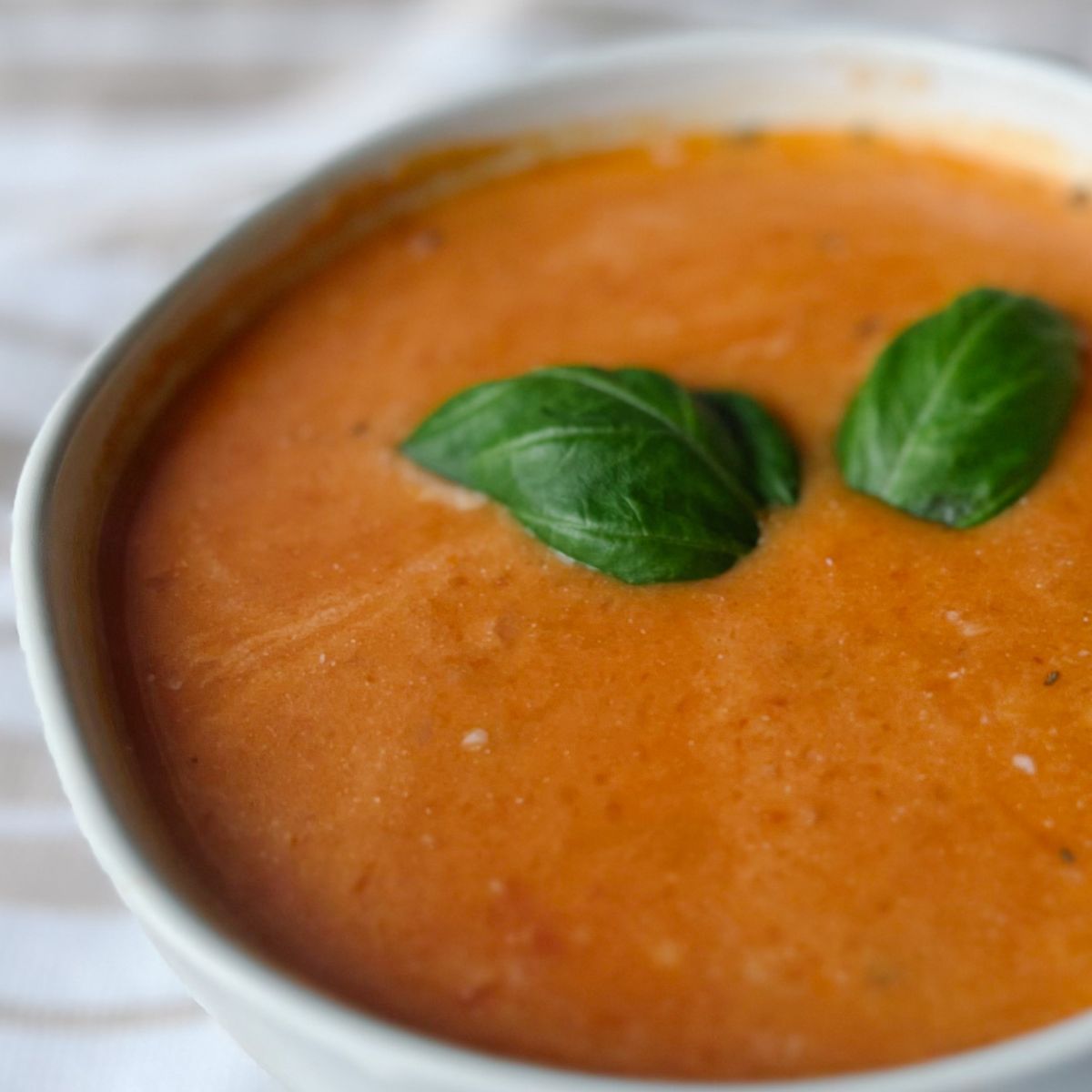 bowl of tomato soup with two basil leaves on top.