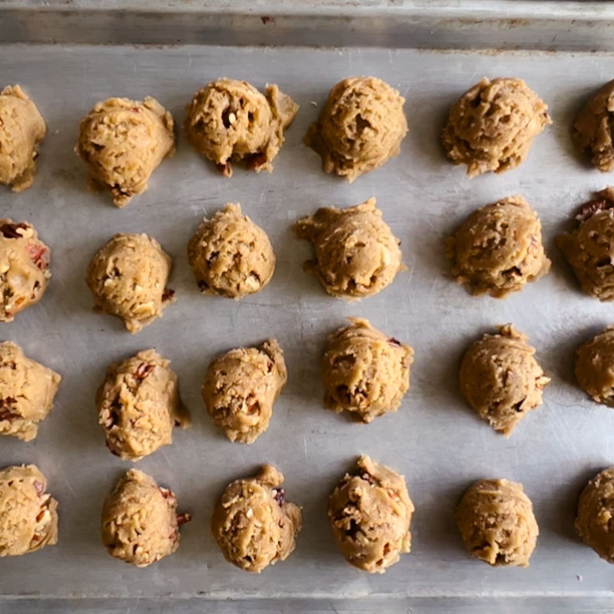 24 cookie dough balls on a baking sheet.
