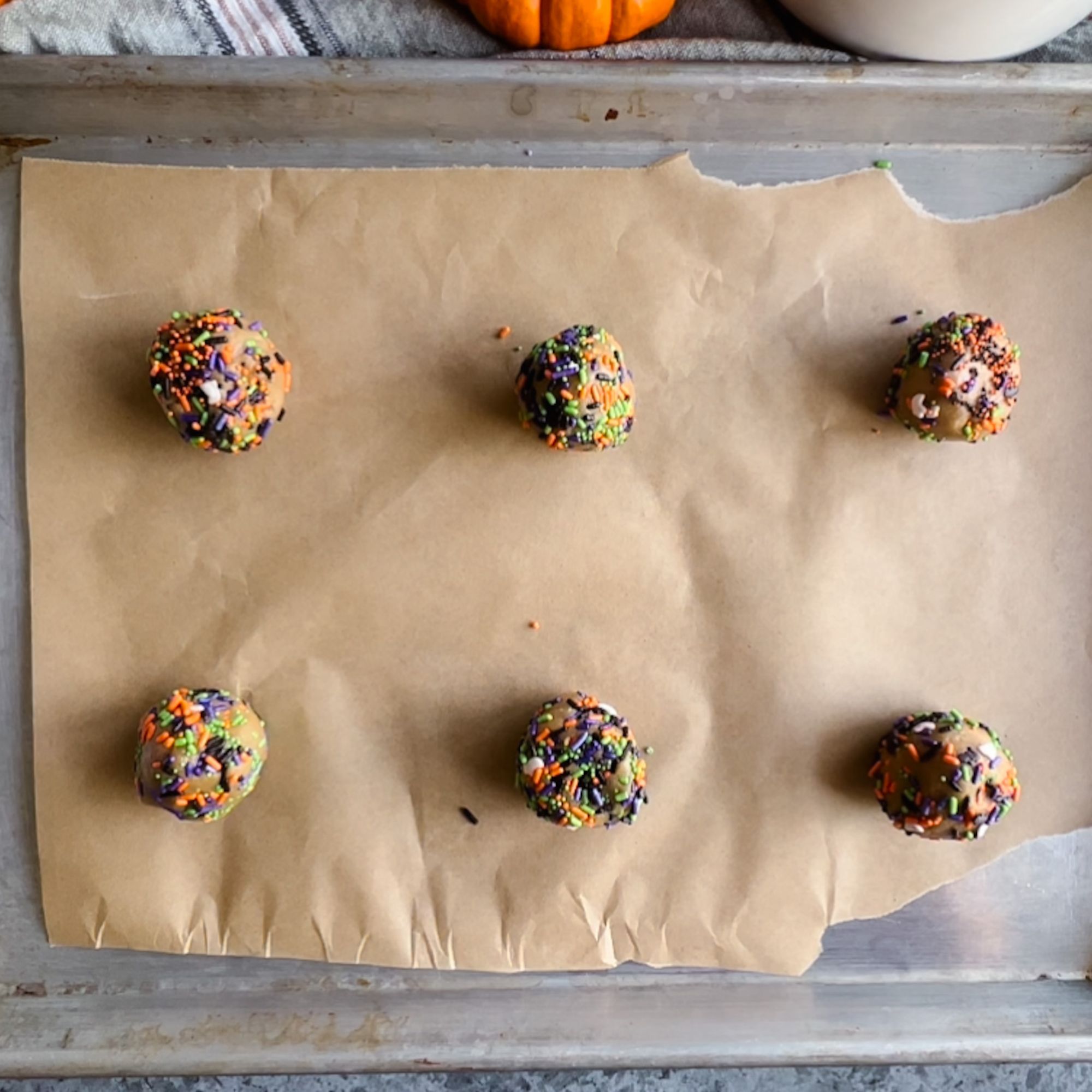 Six cookie dough balls on a parchment lined baking sheet ready to be baked. 