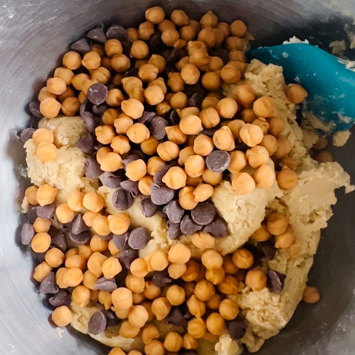 Cookie dough in a mixing bowl with caramel bits and chocolate chips added to it. 