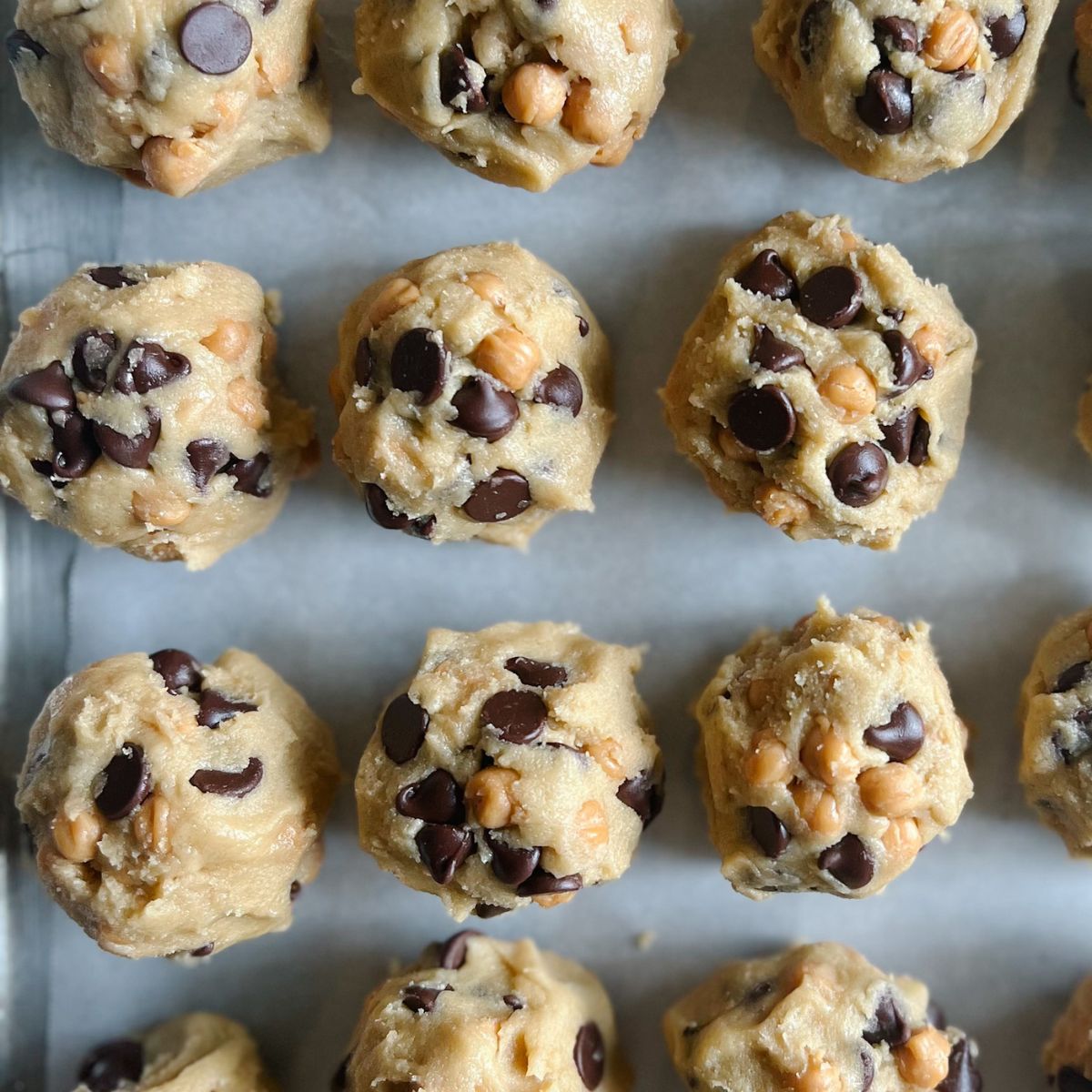 Balls of cookie dough on a parchment paper lined baking sheet. 