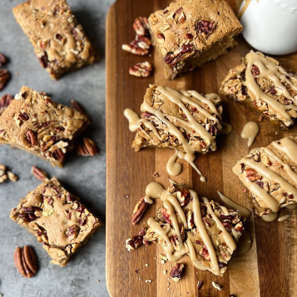 Maple Pecan Blondies with caramel glaze on the cutting board. Three plain blondies on counter.