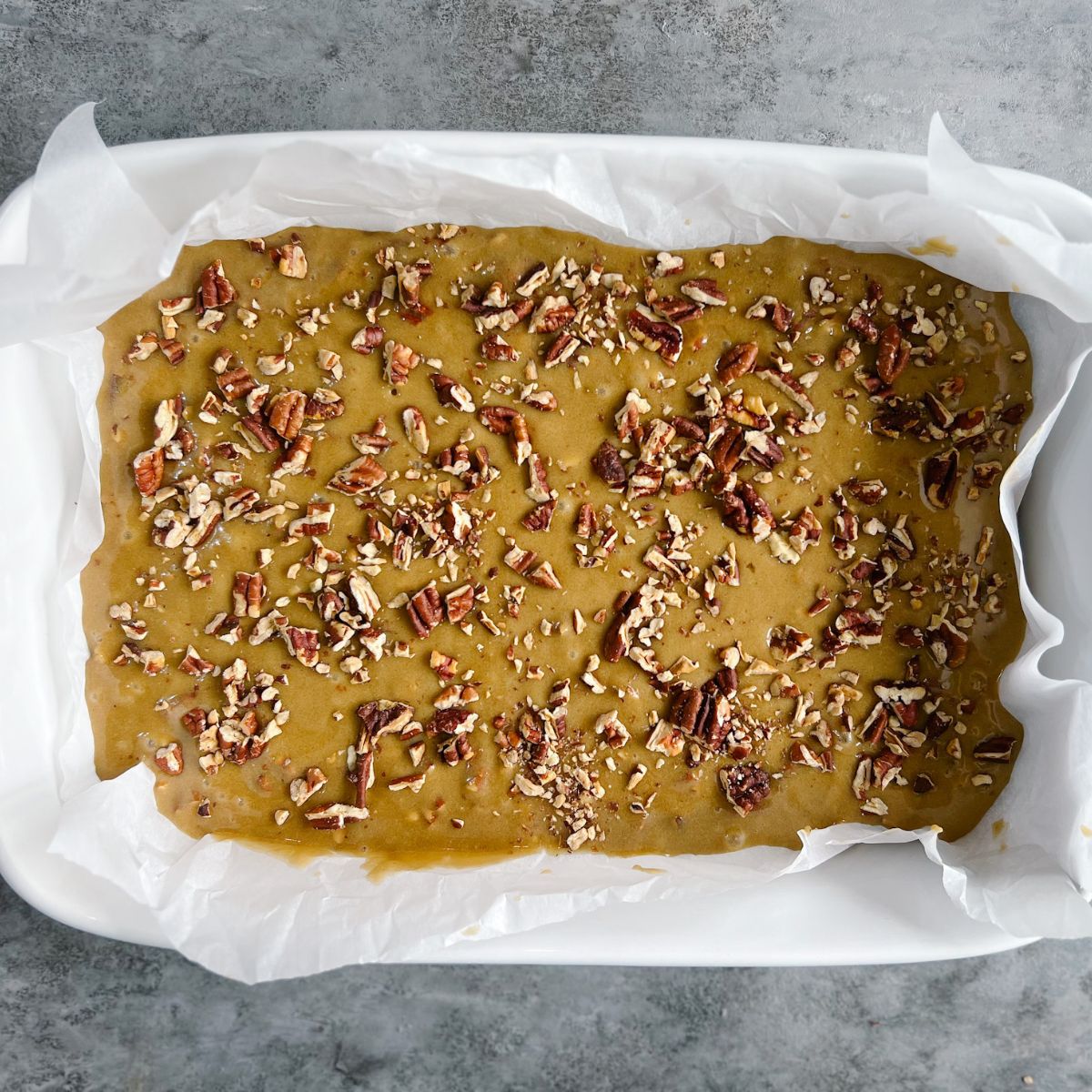 Blondie batter in a parchment paper covered 9x13 baking dish topped with chopped pecans.