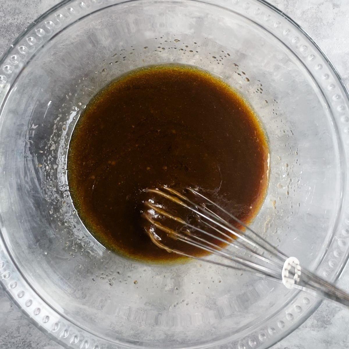 A mixing bowl with olive oil, brown sugar, and maple syrup whisked together.