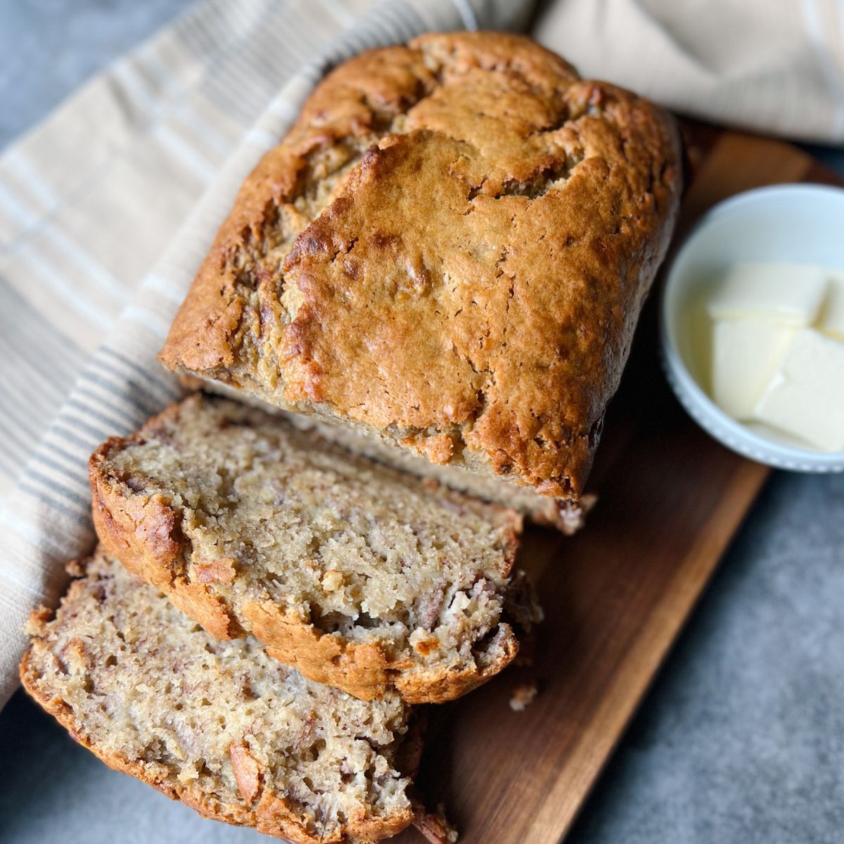 tahini banana bread with two slices cut out. All of it is sitting on a wooden cutting board.