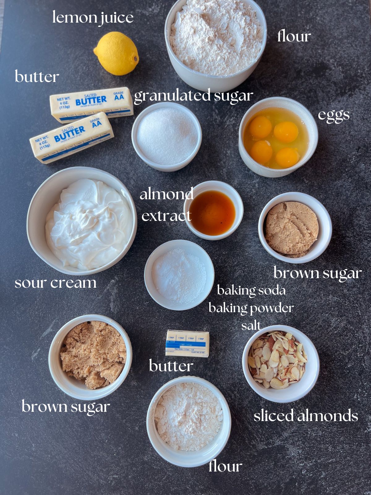 The almond coffee cake ingredients: flour, butter, granulated sugar, brown sugar, butter, almond extract, baking soda, baking powder, salt, lemon juice, sour cream, eggs, sliced almonds.