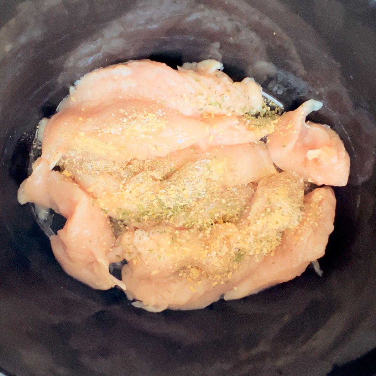 Raw chicken and seasonings in a crockpot. 