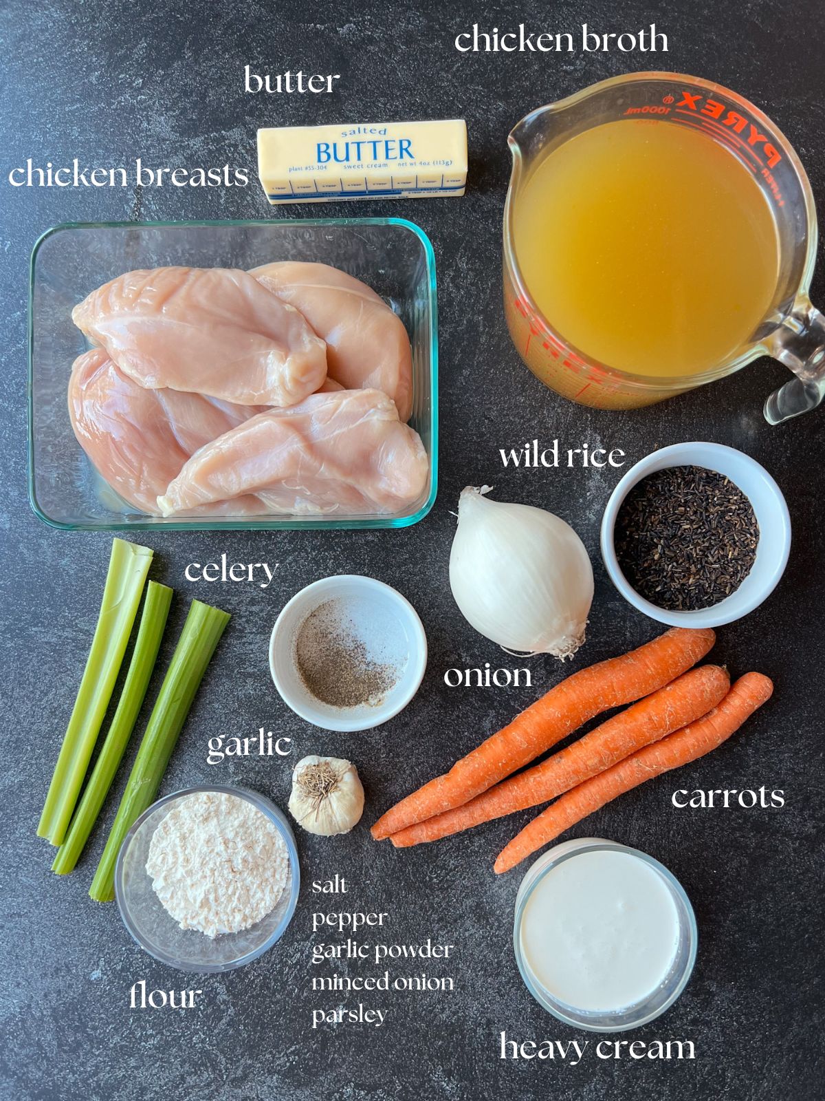 Ingredient shot for chicken wild rice soup: chicken breasts, carrots, celery, onion, flour, salt, pepper, garlic, wild rice, heavy cream, chicken broth.