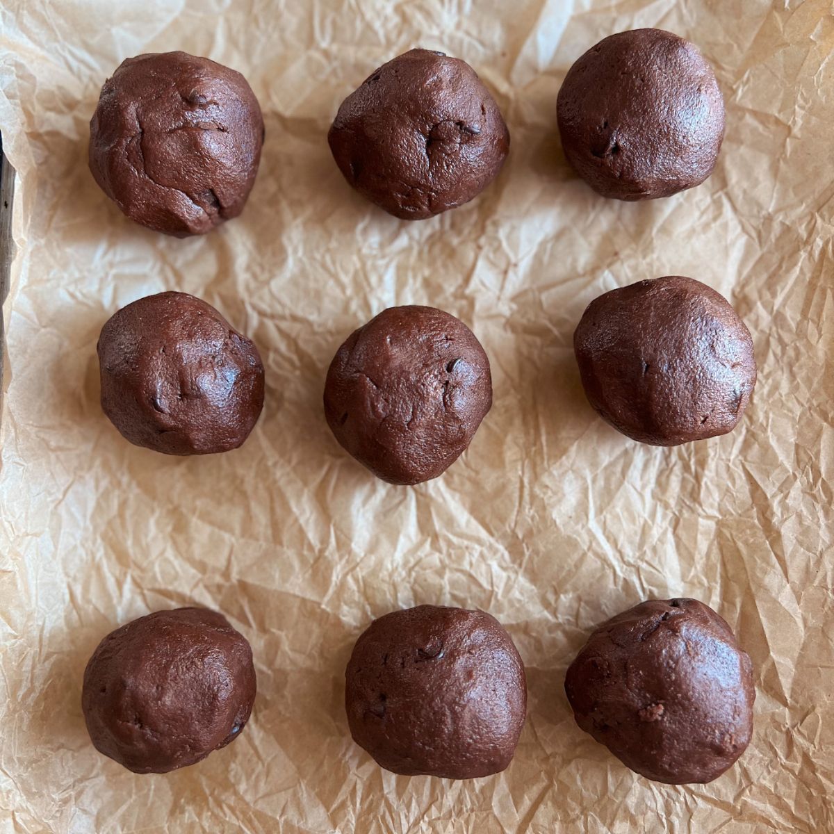 Cookie dough balls rolled and sitting on parchment paper.