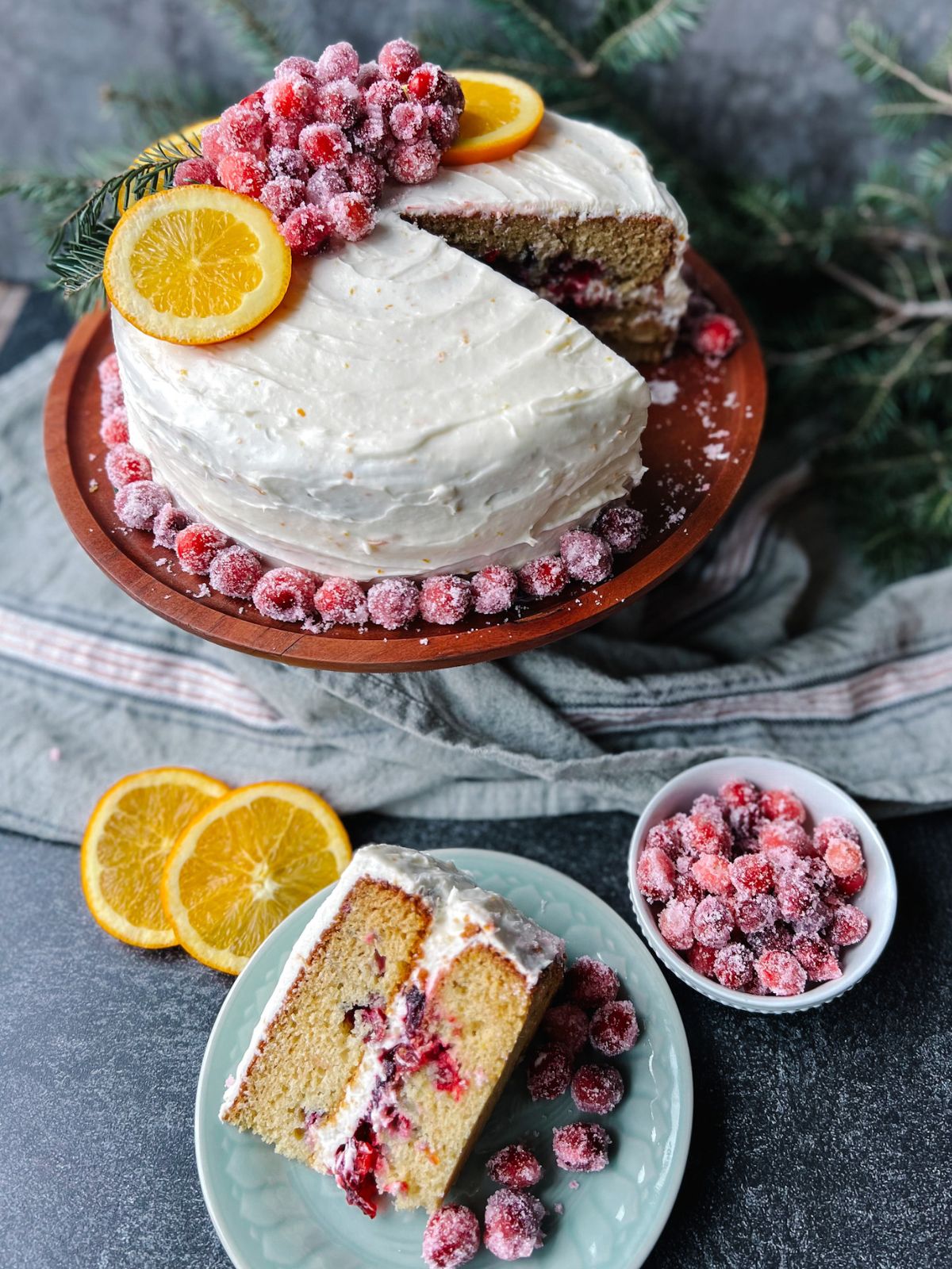 Cranberry orange cake on a wooden cake stand and a slice of cranberry orange cake in front of it. 