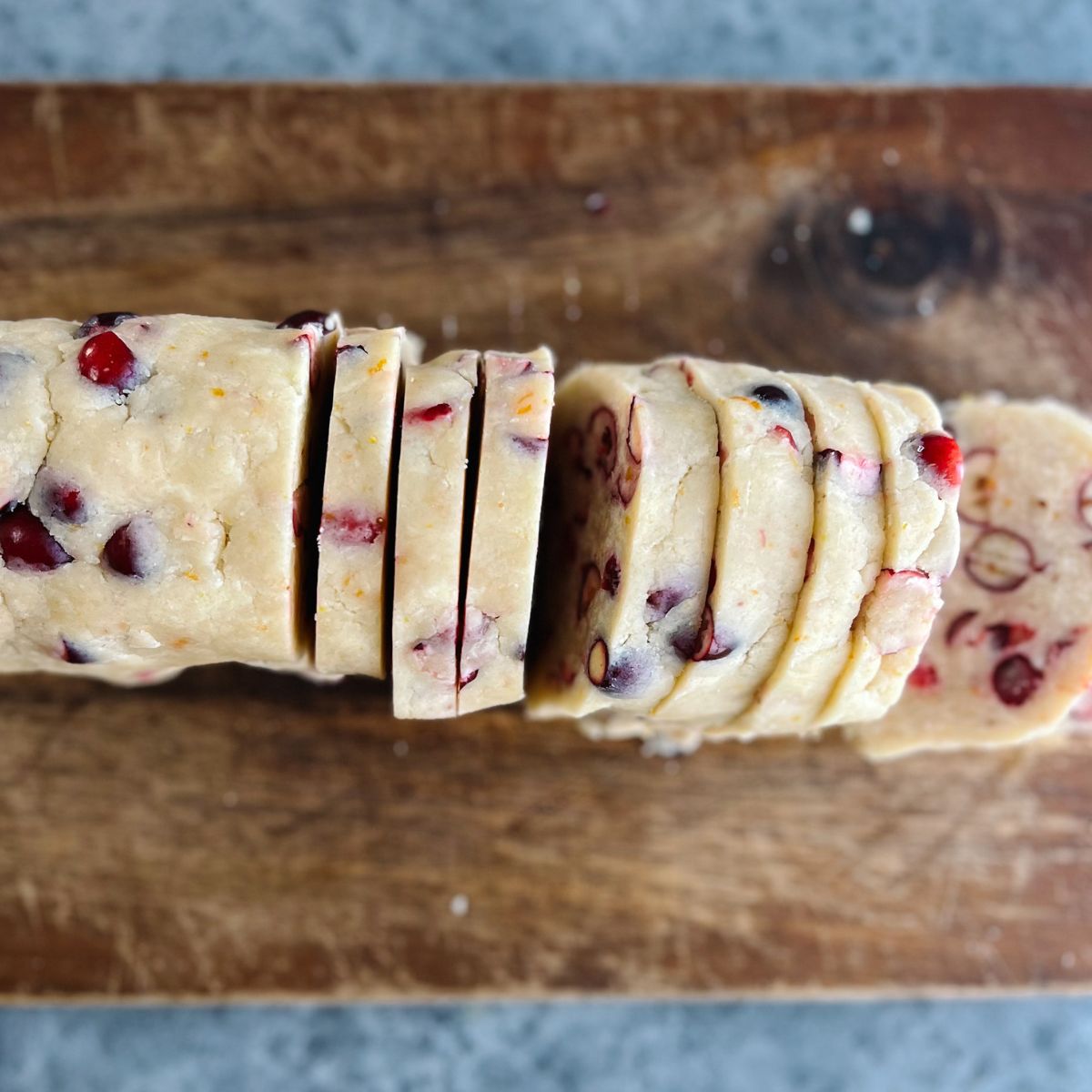Cranberry orange shortbread cookie dough sliced on wooden cutting board.
