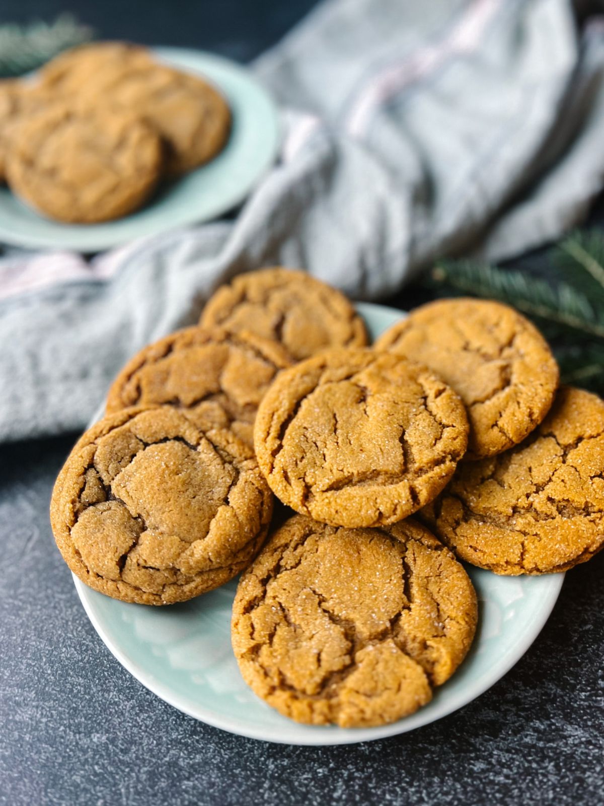 Soft and chewy ginger snap cookies on a plate with a towel between another plate of ginger snap cookies in the background.