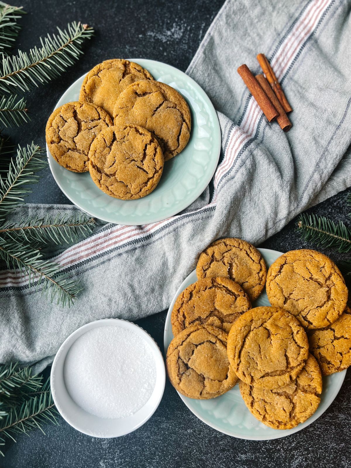 Two plates of ginger snap cookies with a kitchen towel and a bowl of granulated sugar. 
