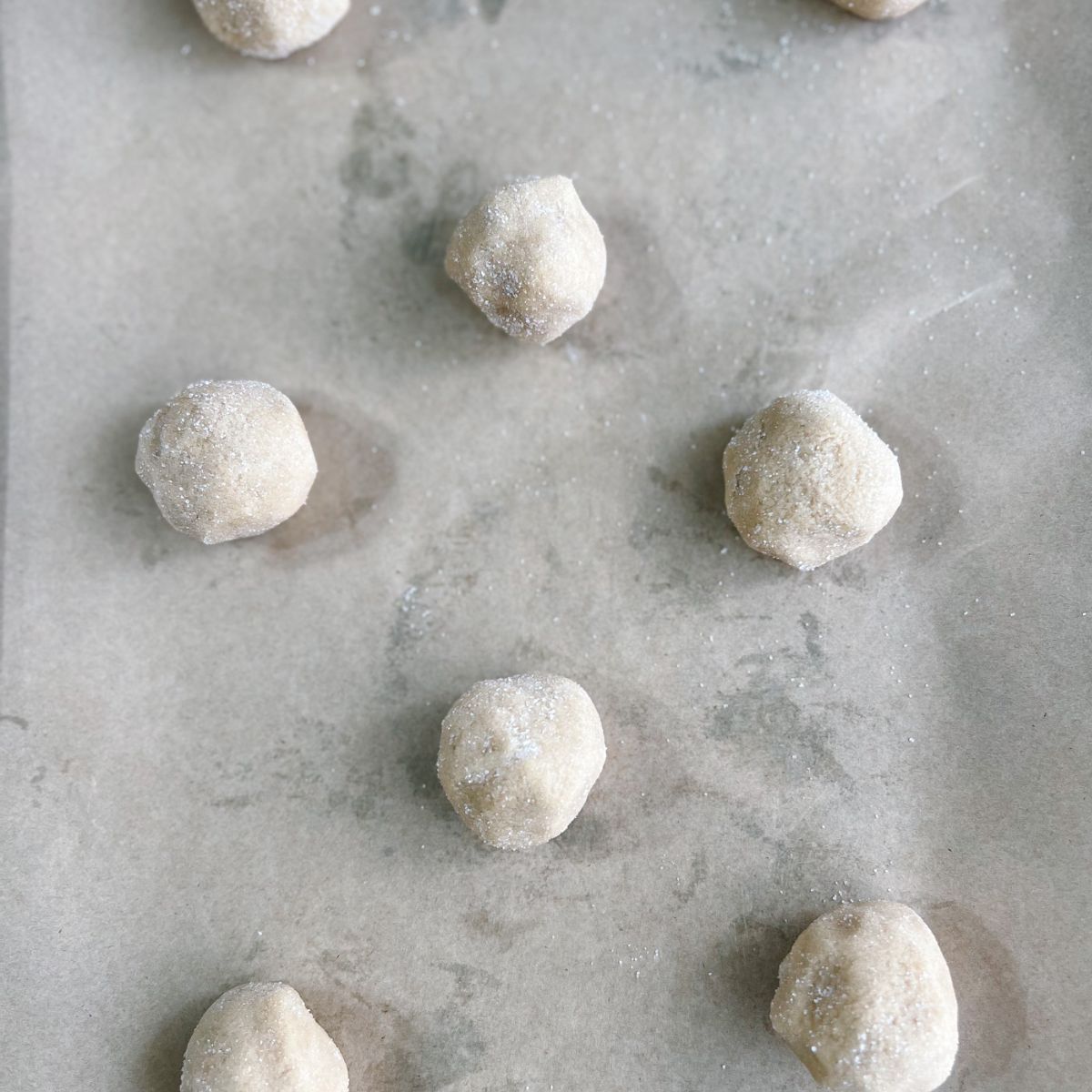 Cookie dough balls on a parchment paper lined baking sheet.