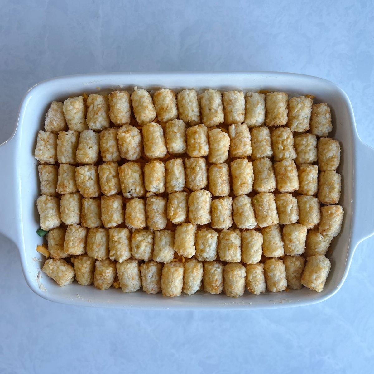Uncooked tater tot hotdish with the tater tots lined evenly on top of the ingredients.