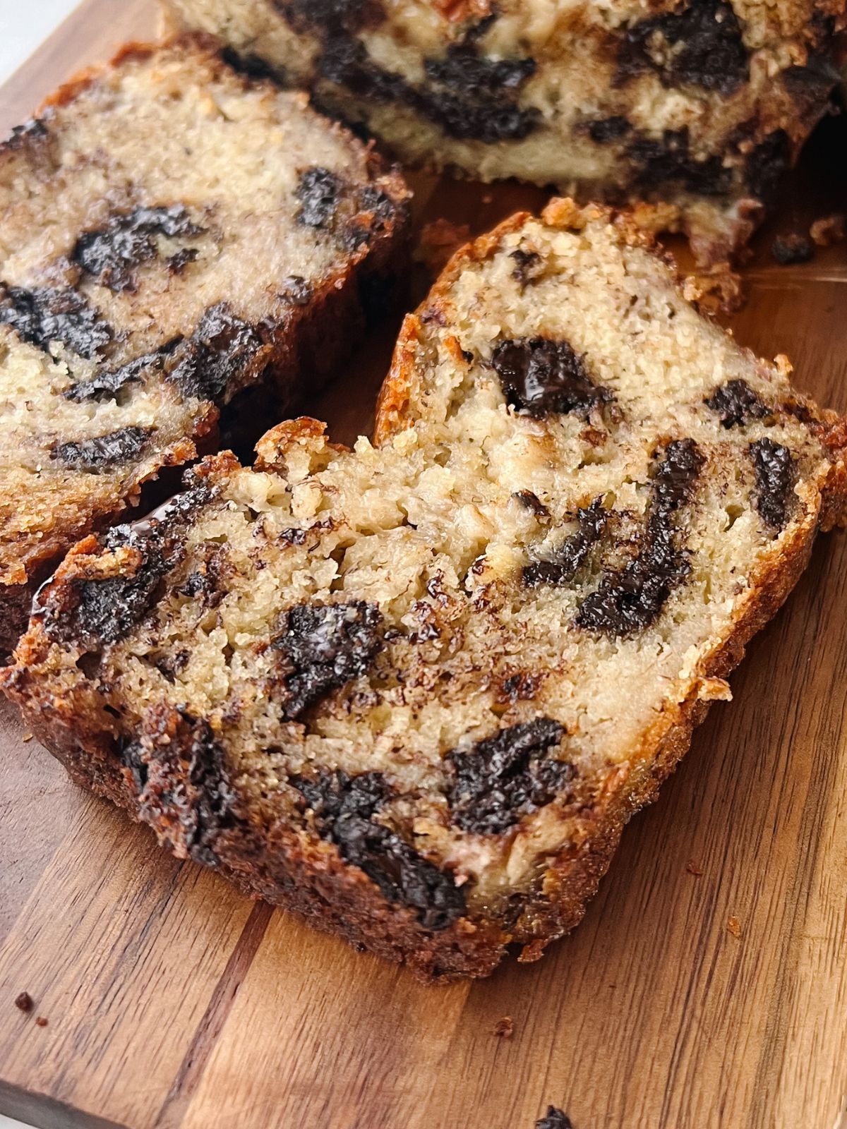 Two slices of chocolate chunk banana bread on a wooden cutting board. 