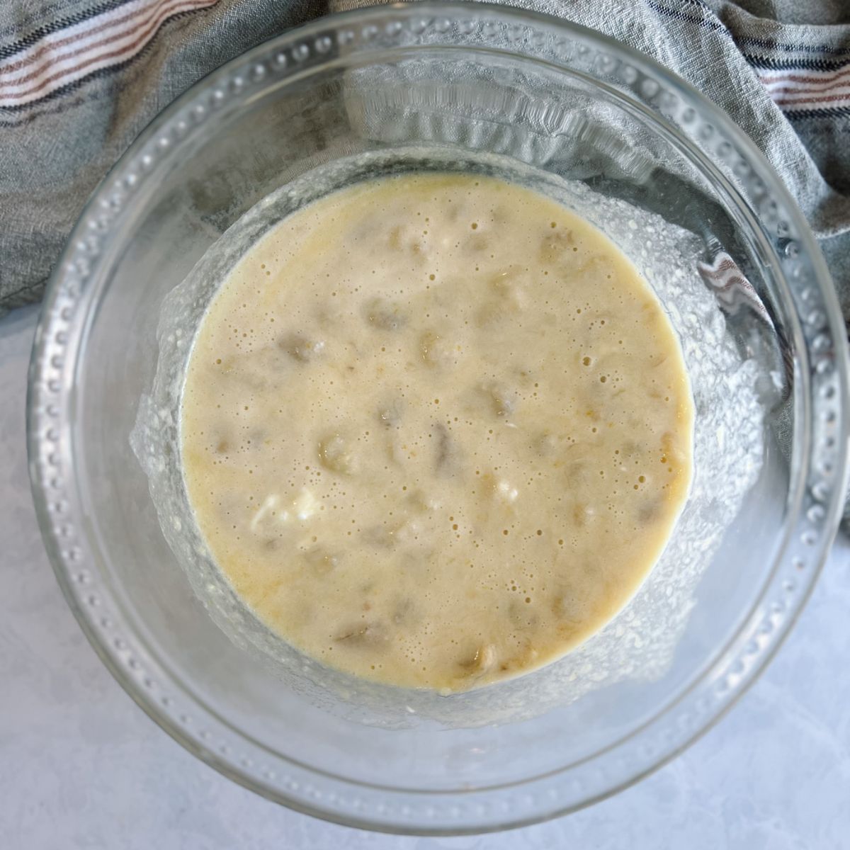 Wet ingredients in a mixing bowl with mashed bananas added to it. 