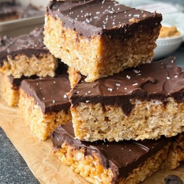 Chocolate peanut butter krispie treats stacked on top of each other while sitting on parchment paper.