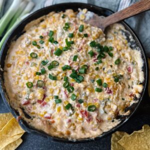 Cast iron skillet of cream cheese corn dip and a wooden spoon in the dip.