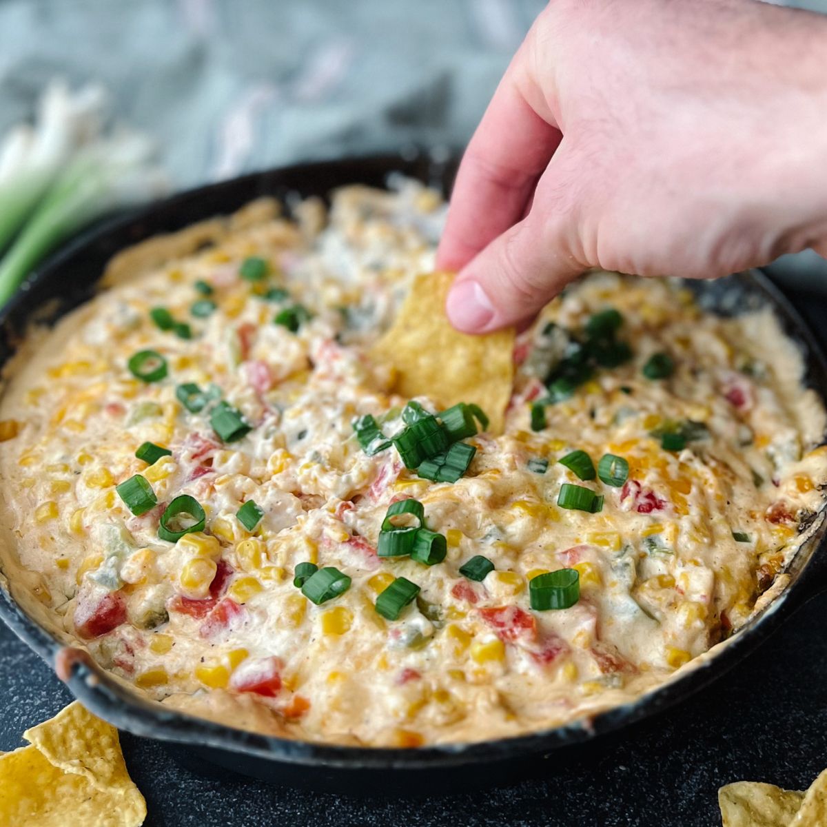 Hand dipping a chip in the skillet of cream cheese corn dip.