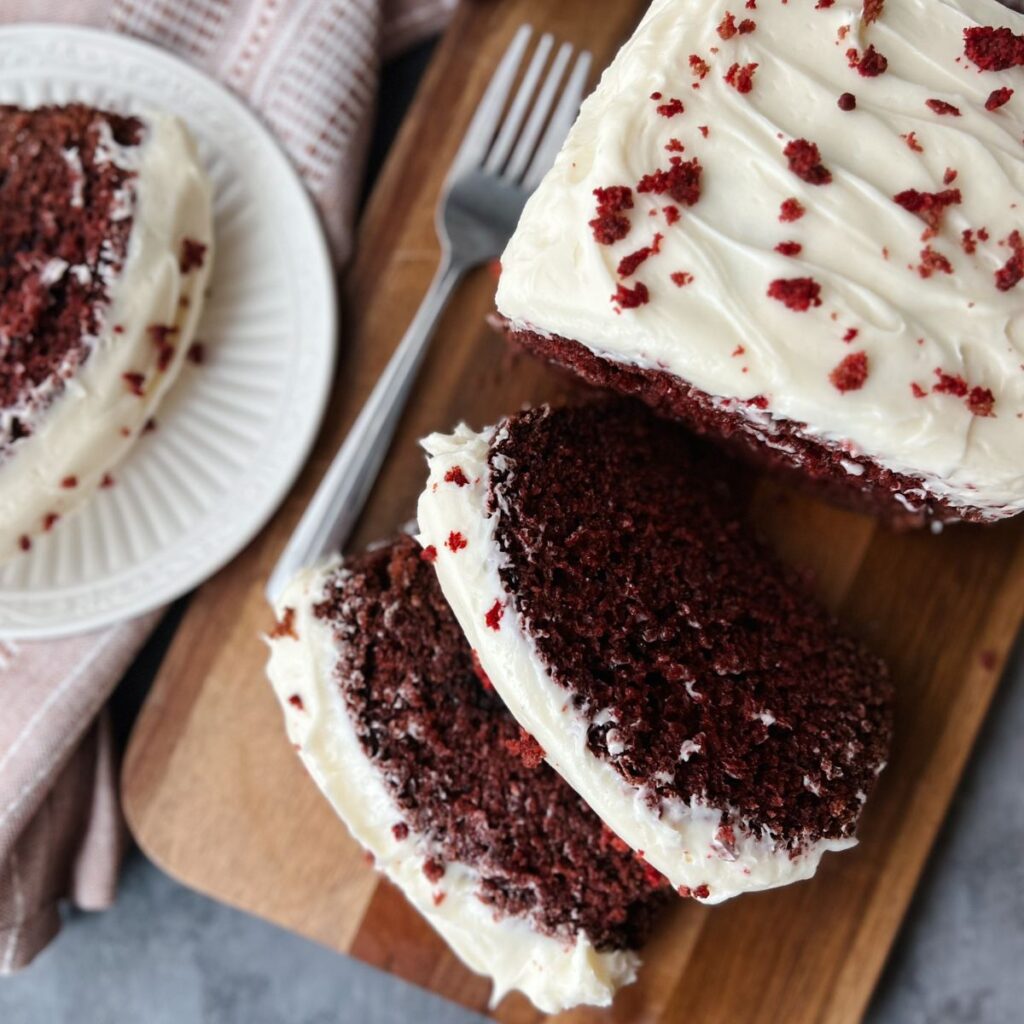 Red velvet loaf cake with two slices cut out and sitting by the cake and another slice on a plate to the side.