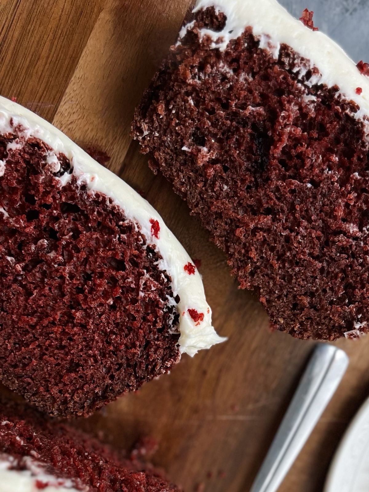 Two slices of red velvet cake on a wooden cutting board.