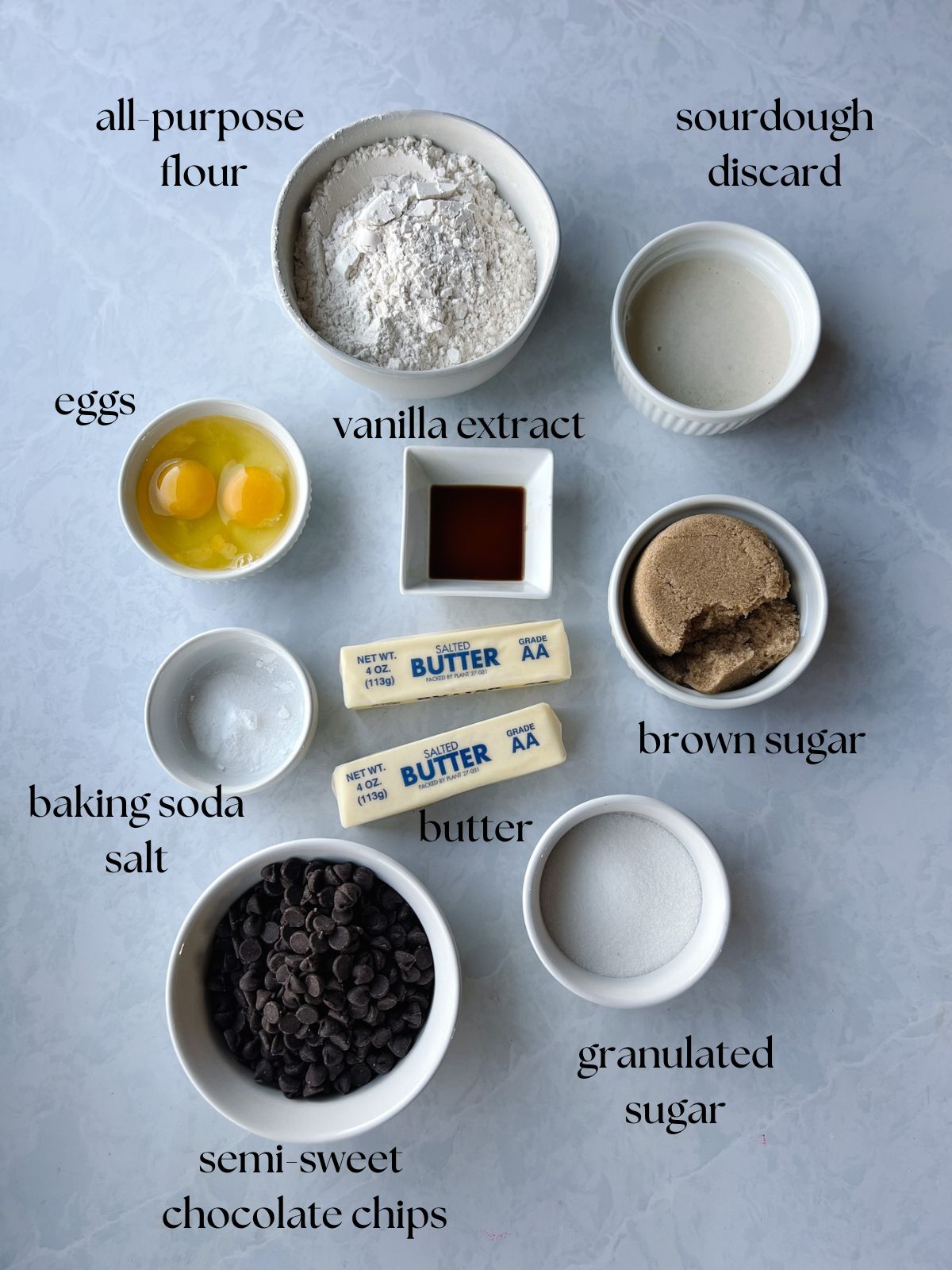Picture of ingredients needed for sourdough chocolate chip cookies. All-purpose flour, sourdough discard, vanilla extract, eggs, butter, brown sugar, granulated sugar, baking soda, salt, semi-sweet chocolate chips.
