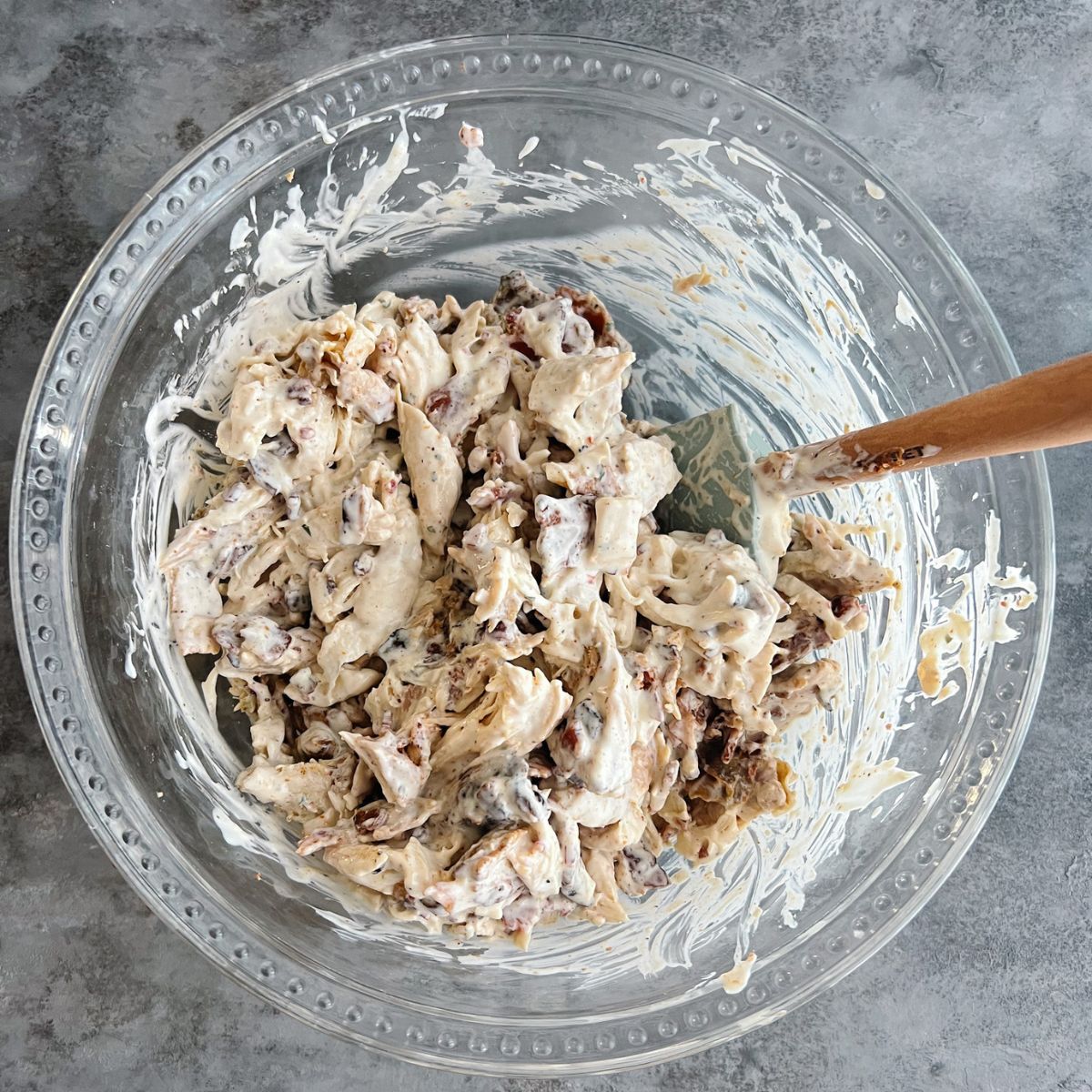 Shredded chicken, bacon, and ranch mixed together in a mixing bowl with a rubber spatula in it.