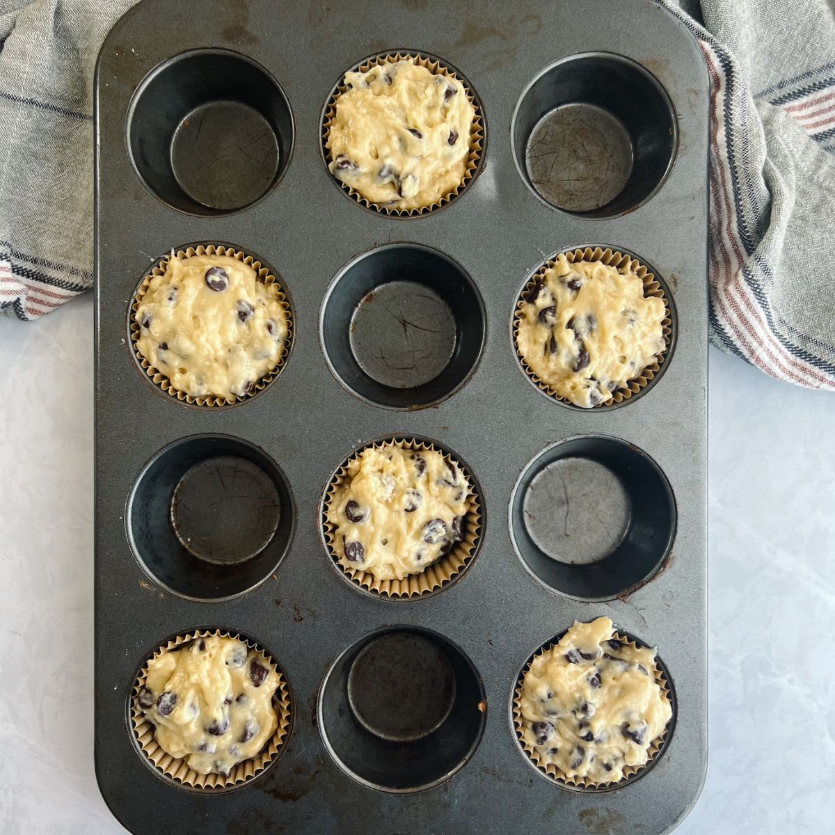 Muffin tin with every other muffin hole filled with muffin liner and batter.