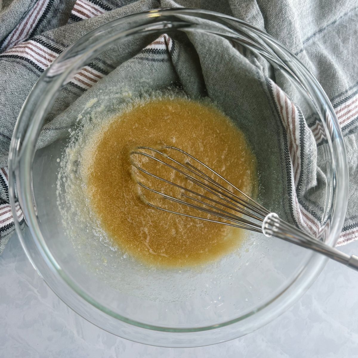 Mixing bowl with a whisk in and melted butter and sugars in the bowl.