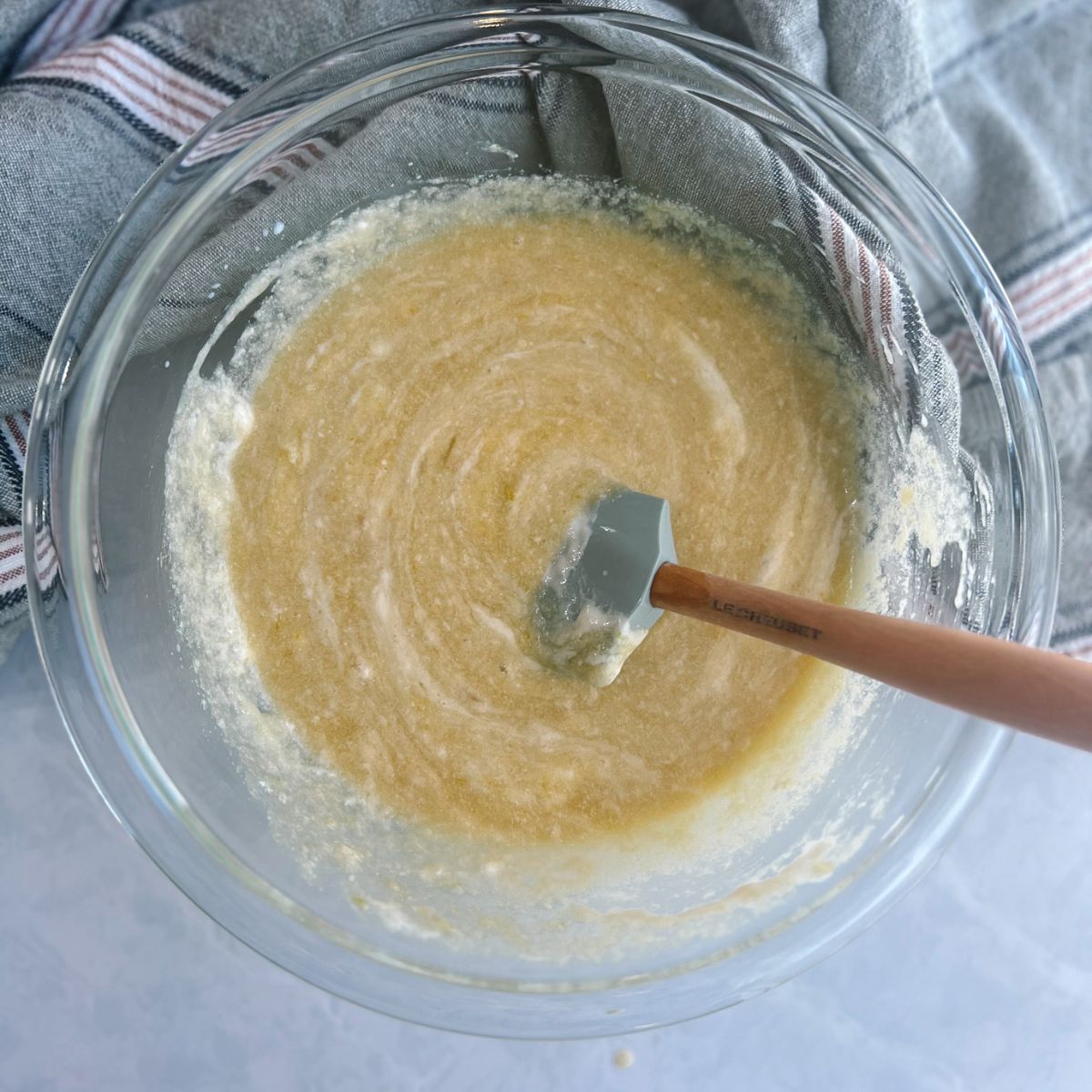 Glass mixing bowl with a rubber spatula and the buttermilk, egg, vanilla extract, and sourdough discard has been added to the muffin batter.
