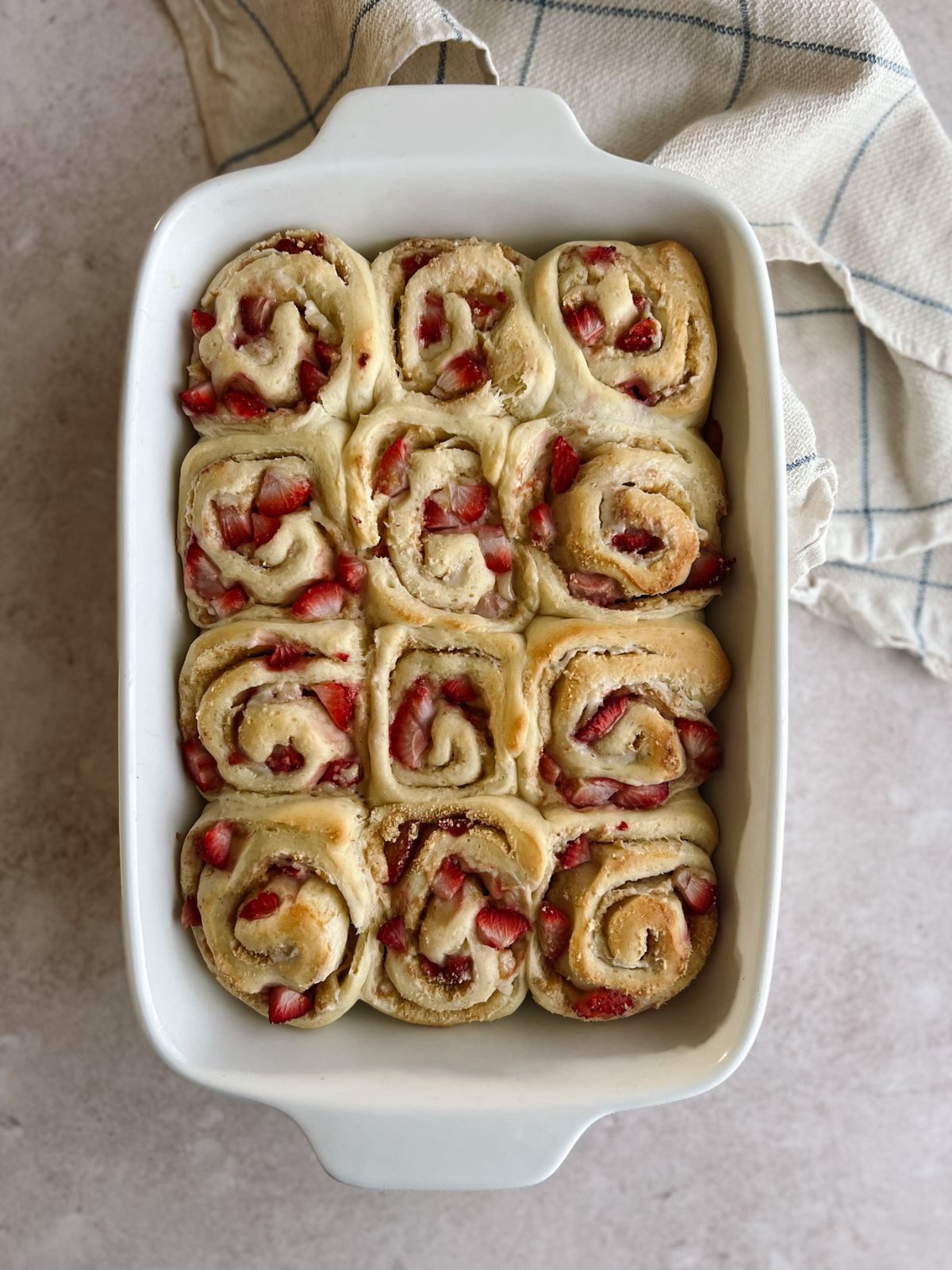 Baked and unfrosted strawberry cheesecake cinnamon rolls in the baking pan.