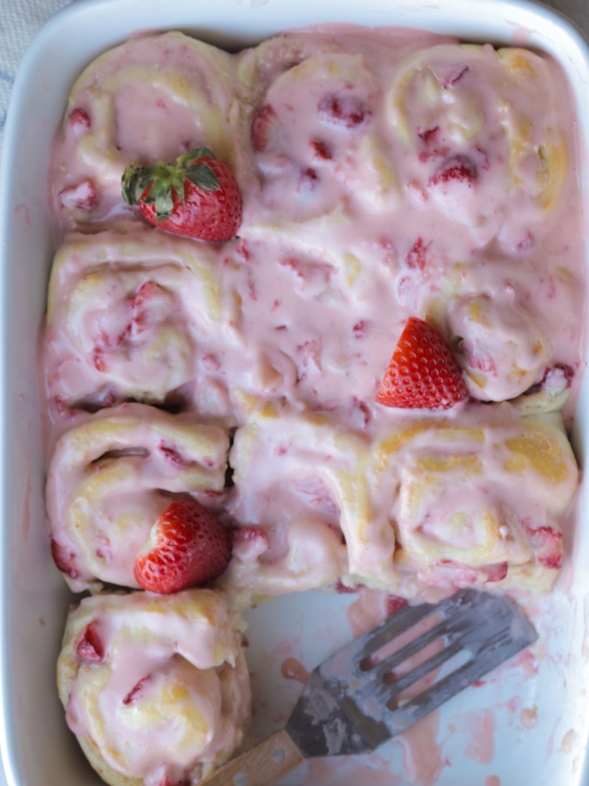 Strawberry cheesecake cinnamon rolls with strawberry icing and a few strawberries on top of them for decoration.