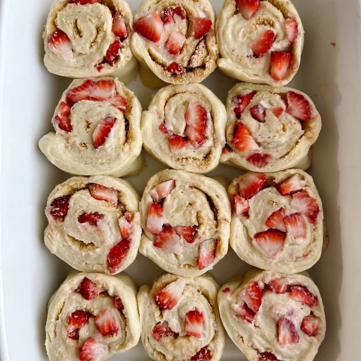 Twelve Unbaked strawberry cinnamon rolls in the baking dish. 