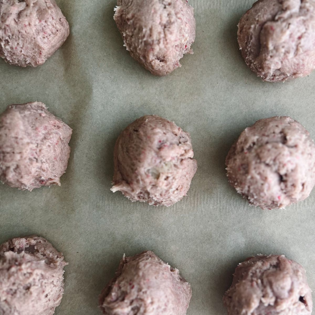 Strawberry crunch cookie dough balls on a parchment paper-lined baking sheet ready to be chilled in the fridge.