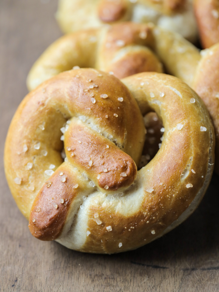 Homemade sourdough pretzel with several in the background. It's golden brown and topped with coarse salt.