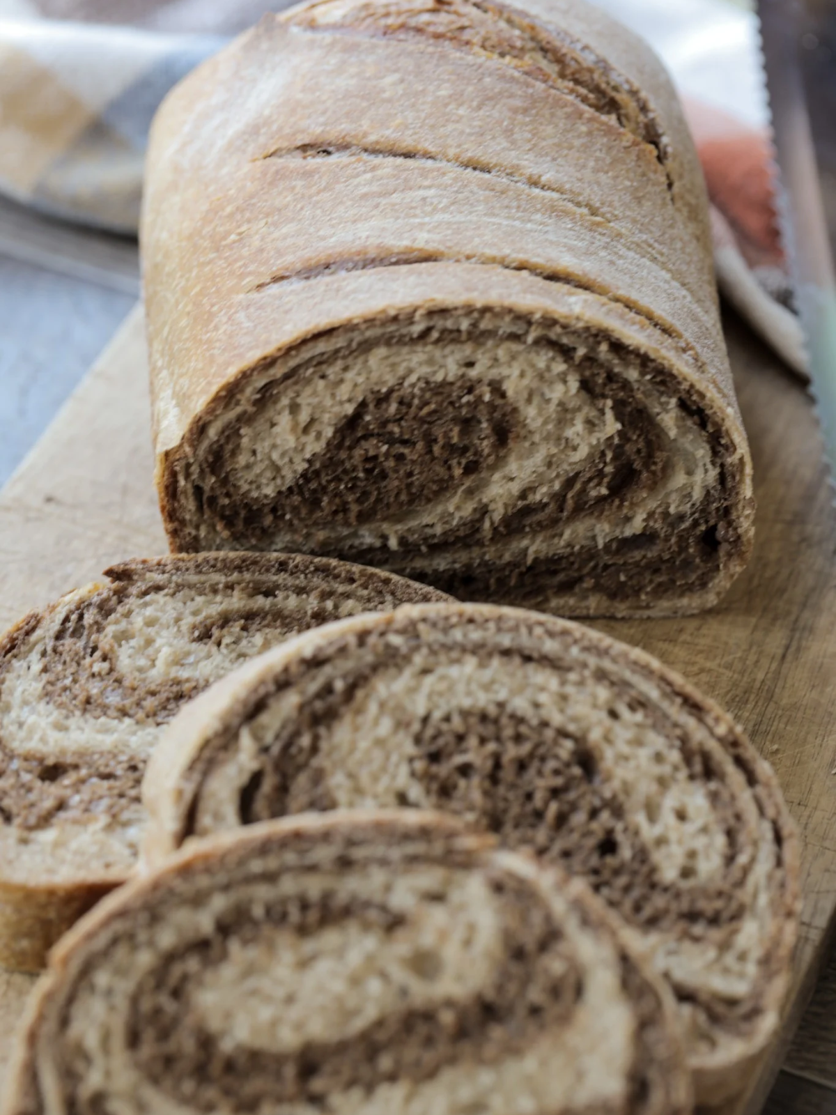The loaf of the swirled marble rye sourdough bread and a couple slices lay on a wooden cutting board.