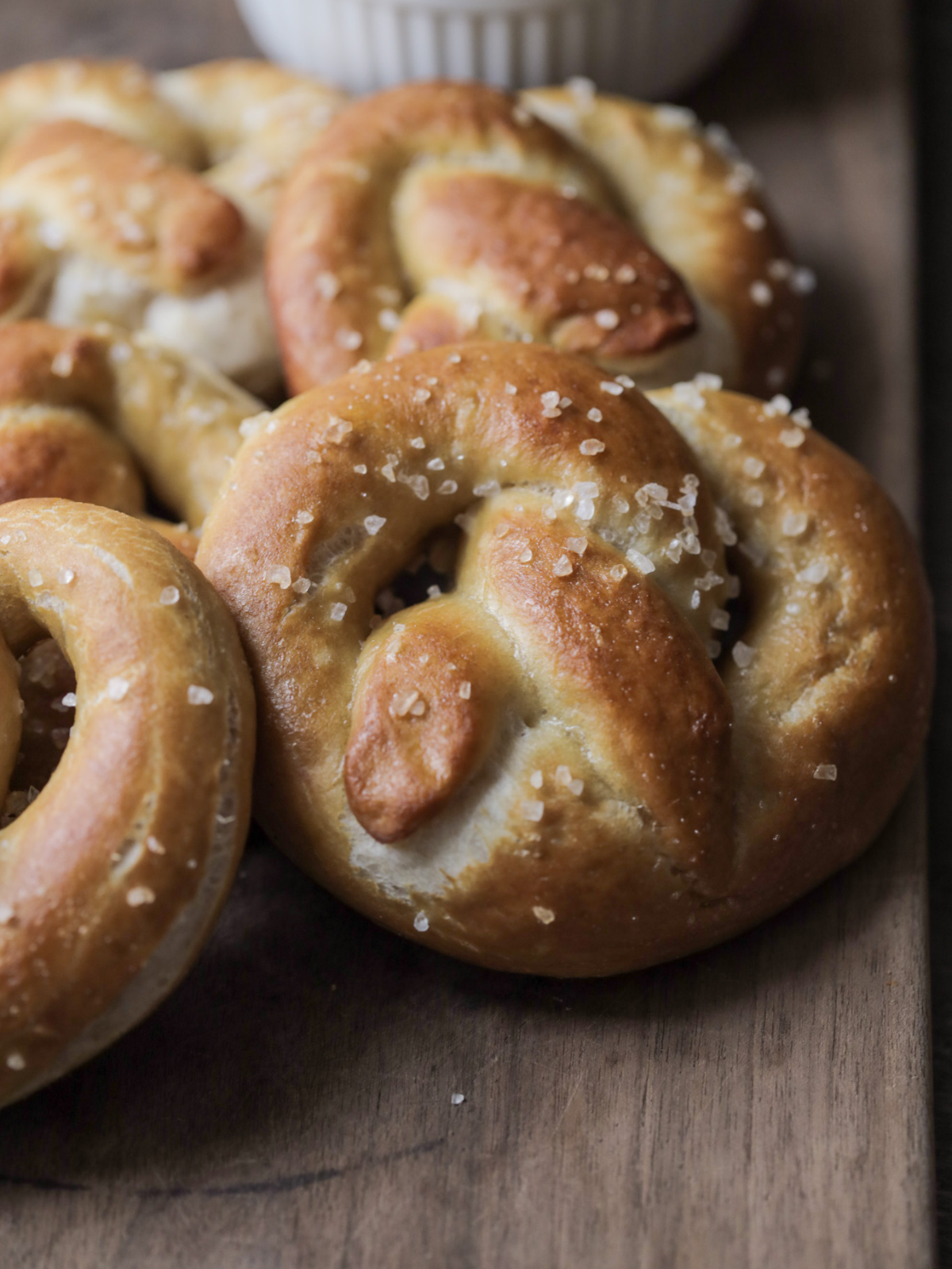 Several homemade sourdough pretzels with coarse salt. Beer cheese dipping sauce sits in the background.