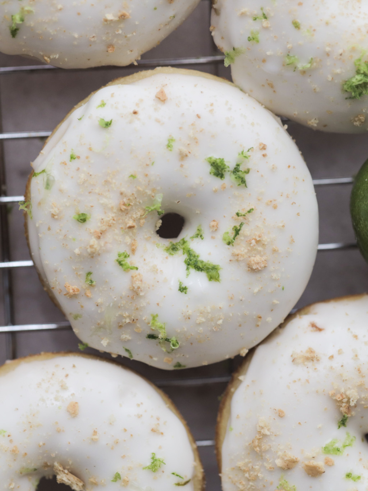 A closeup picture of a single key lime sourdough donut sitting on a wire rack. It's surrounded by other doughnuts.